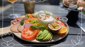 Una tabla de madera con rodajas de tomate, aguacate y diferentes carnes.
