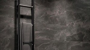 Un baño moderno con una pared de mármol oscuro, un perchero negro con una toalla y un mueble de madera.