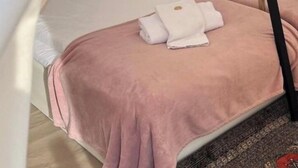 Una cama individual con una manta rosa y almohadas blancas, una escalera negra y un dosel blanco.