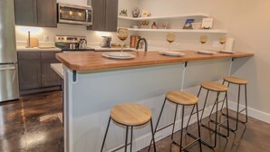 A modern kitchen with a central island, bar stools, and stainless steel appliances. - Hundred Mullet Hotel- New Home Near Foley  (Foley)