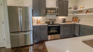 A modern kitchen with stainless steel appliances, dark cabinetry, and white countertops. - Hundred Mullet Hotel- New Home Near Foley  (Foley)