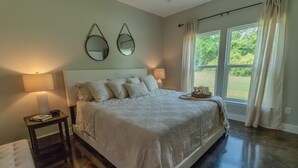 A bedroom with a large bed, two bedside lamps, a nightstand, and a window with curtains. - Hundred Mullet Hotel- New Home Near Foley  (Foley)