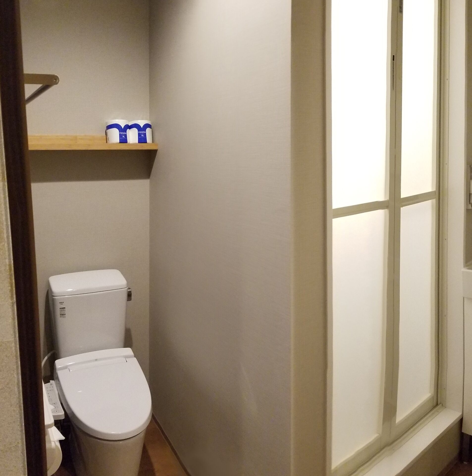 Un baño pequeño con inodoro, un estante con artículos de tocador y una ventana.