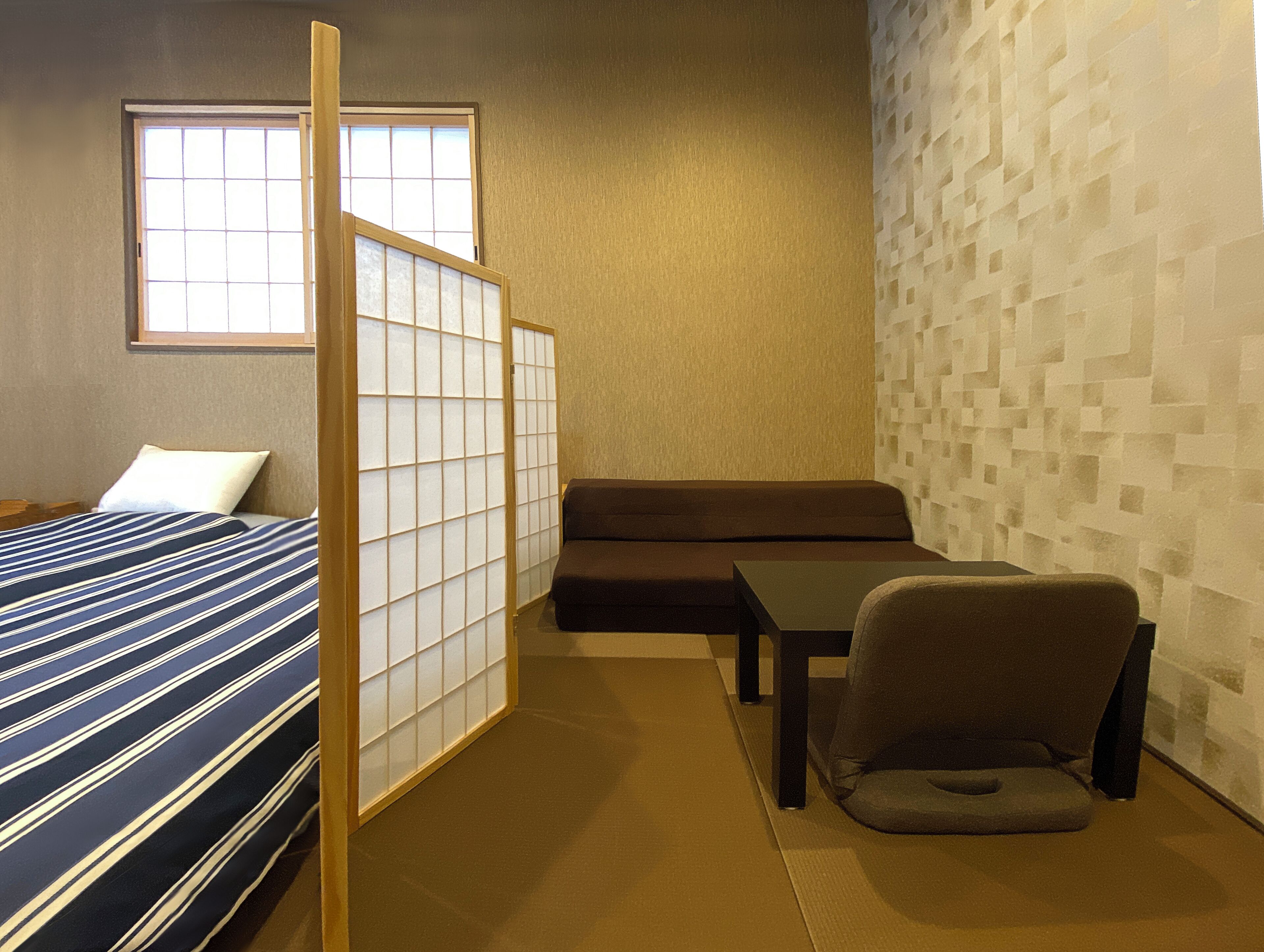 A compact hotel room with a bed, a sofa, a small table, and a chair.