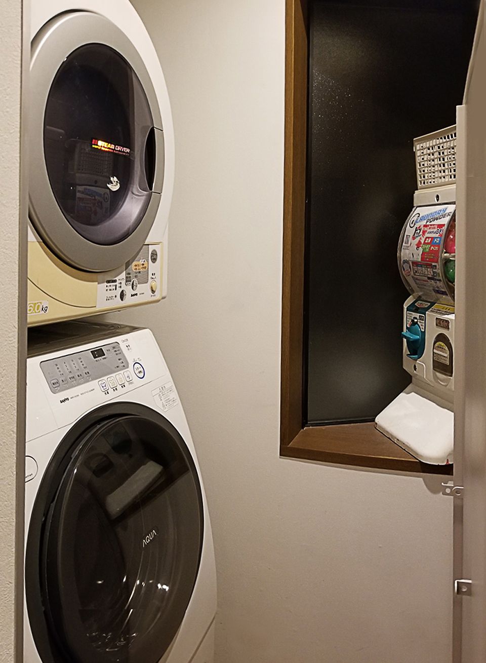 A laundry room with a front-loading washing machine, a dryer, and a small window with a toilet and a trash can.