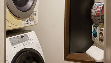 A laundry room with a front-loading washing machine, a dryer, and a small window with a toilet and a trash can.