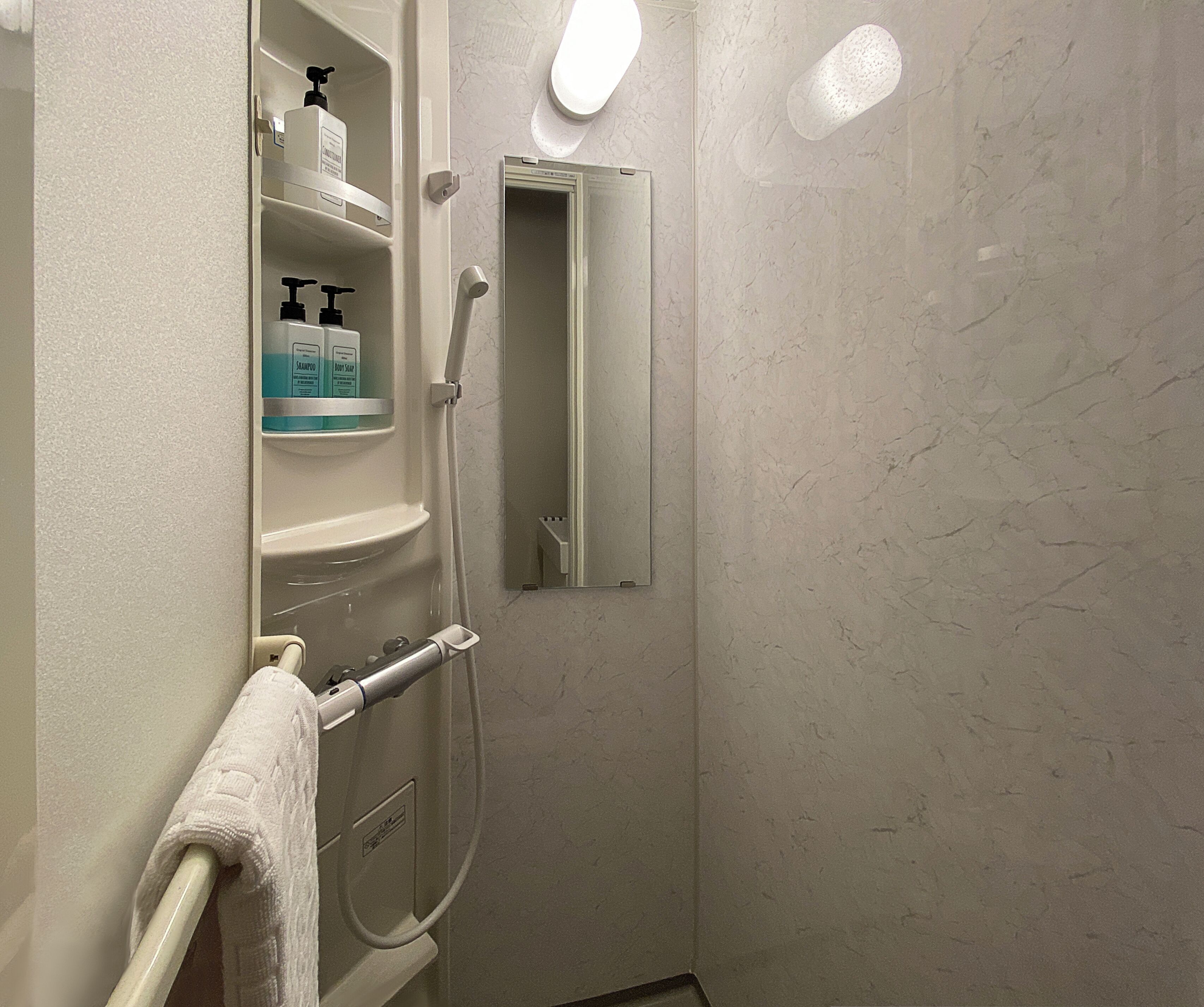 A bathroom with a white towel hanging on a rack, a shelf with toiletries, and a mirror.