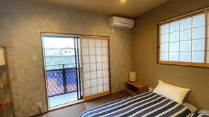 A bedroom with a bed, a nightstand, a window, and an air conditioning unit. - My Home Inn Izumisano (Izumisano)