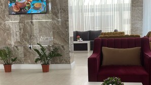 Ein modernes Wohnzimmer mit Marmorwand, Flachbildfernseher, rotem Sofa und zwei Zimmerpflanzen.