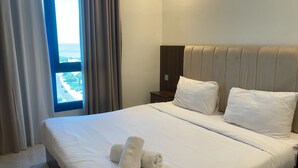 Ein Hotelzimmer mit einem großen Bett, zwei Kissen, einem Nachttisch und einem Fenster mit Vorhängen.
