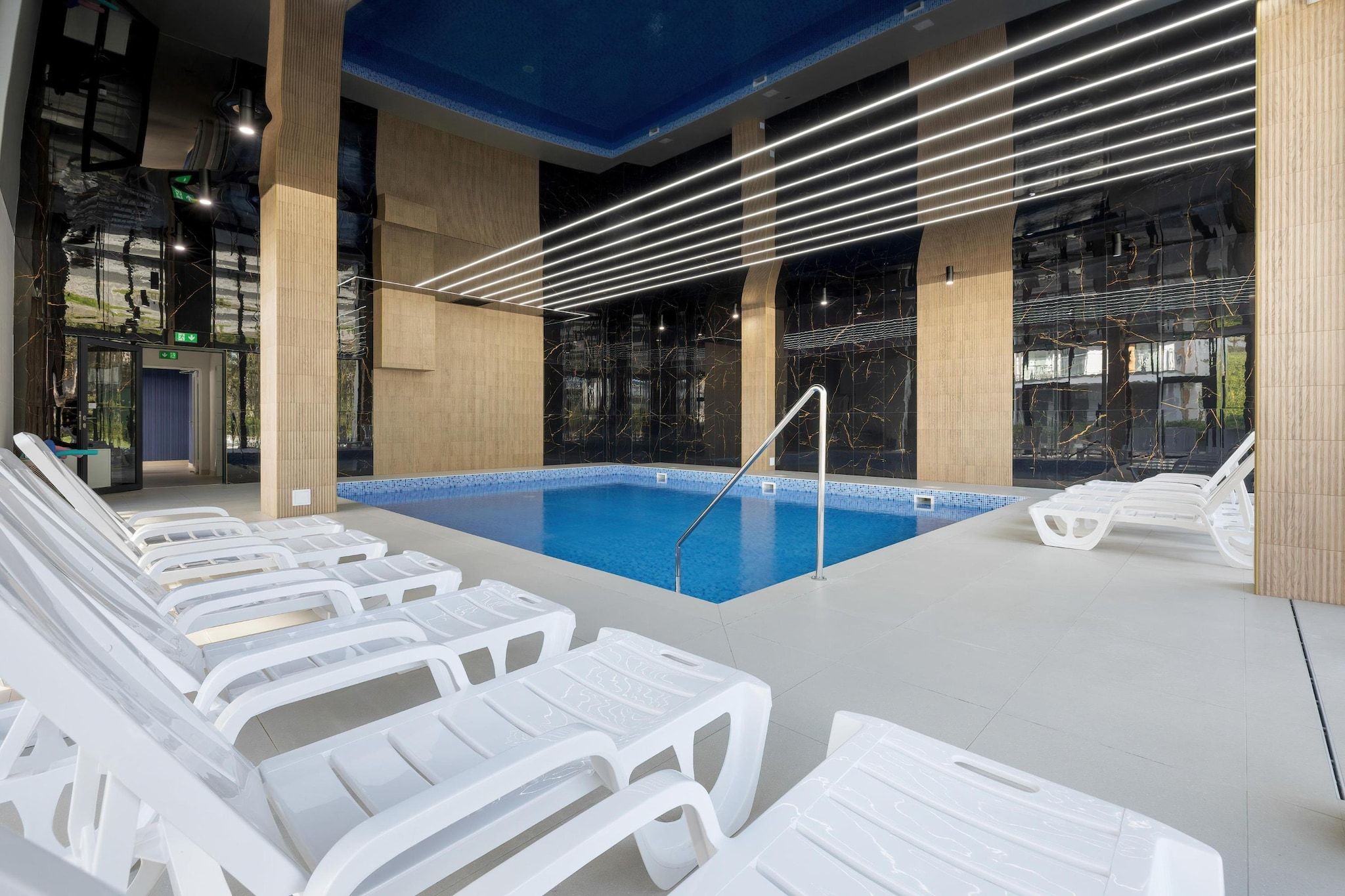 Ein Innenpool mit klarem, blauem Wasser, umgeben von weißen Liegestühlen und einem modernen Deckenbau.