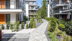 En modern bostadsbyggnad med flera balkonger, en central gångväg och välanlagda trädgårdar.