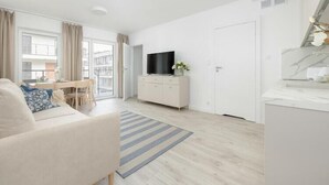 Ett modernt vardagsrum med en soffa, en tv placerad på en tv-bänk, en matplats med ett bord och stolar samt ett stort fönster med gardiner.