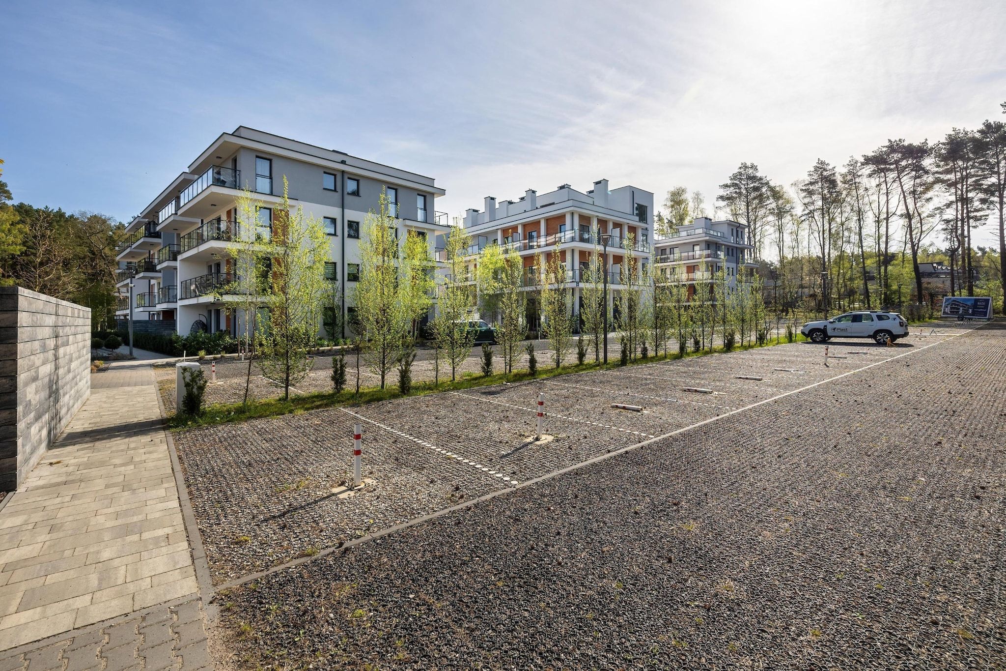 Ein mehrstöckiges Wohngebäude mit Balkonen, einem Kiesparkplatz und jungen Bäumen.