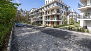 Ett modernt lägenhetskomplex med flera balkonger, en asfalterad uppfart och en bil parkerad vid sidan av.