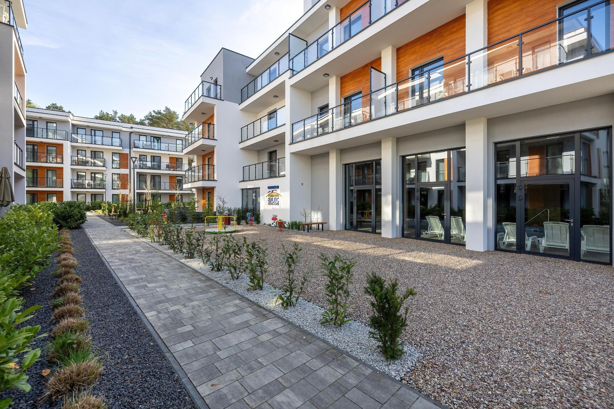 Ein modernes, mehrgeschossiges Wohngebäude mit Balkonen, einem gepflasterten Weg und einem angelegten Garten.