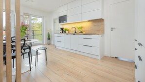 A modern kitchen with white cabinetry, a wooden countertop, and a built-in oven. There is a dining area with a table and chairs, and a small stool. - Comfortable apartment, pool, close to the beach (Pobierowo)
