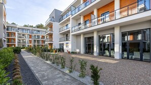A modern apartment building with multiple balconies, a paved walkway, and a landscaped garden area. - Comfortable apartment, pool, close to the beach (Pobierowo)
