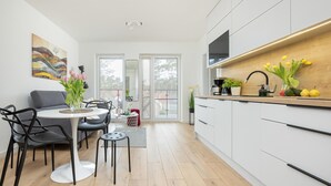 A modern kitchen with white cabinets, a wooden countertop, and a dining area with a round table and chairs. - Comfortable apartment, pool, close to the beach (Pobierowo)