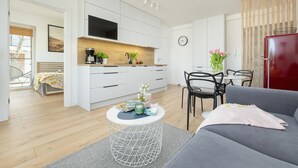 A modern living room with a grey sofa, a round coffee table, and a dining area with a red refrigerator. - Comfortable apartment, pool, close to the beach (Pobierowo)