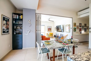 A dining area with a table set for four, chairs, a television mounted on the wall, and a bookshelf with various items.