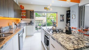 A modern kitchen with granite countertops, a gas stove, and a dining area with a view of the outdoors. - Casa Elizabeth Taylor | Rooftop Pool & Gym (Puerto Vallarta)