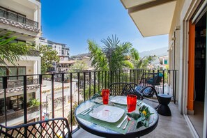 Un balcón con una mesa dispuesta para dos, con vistas a un paisaje urbano con edificios y palmeras.