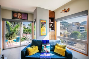 Una sala de estar moderna con un sofá azul, cojines amarillos y un ventanal con vistas a la ciudad.