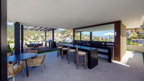 A rooftop bar with a view of a hillside town, outdoor seating, and a pool. - Casa Elizabeth Taylor | Rooftop Pool & Gym (Puerto Vallarta)