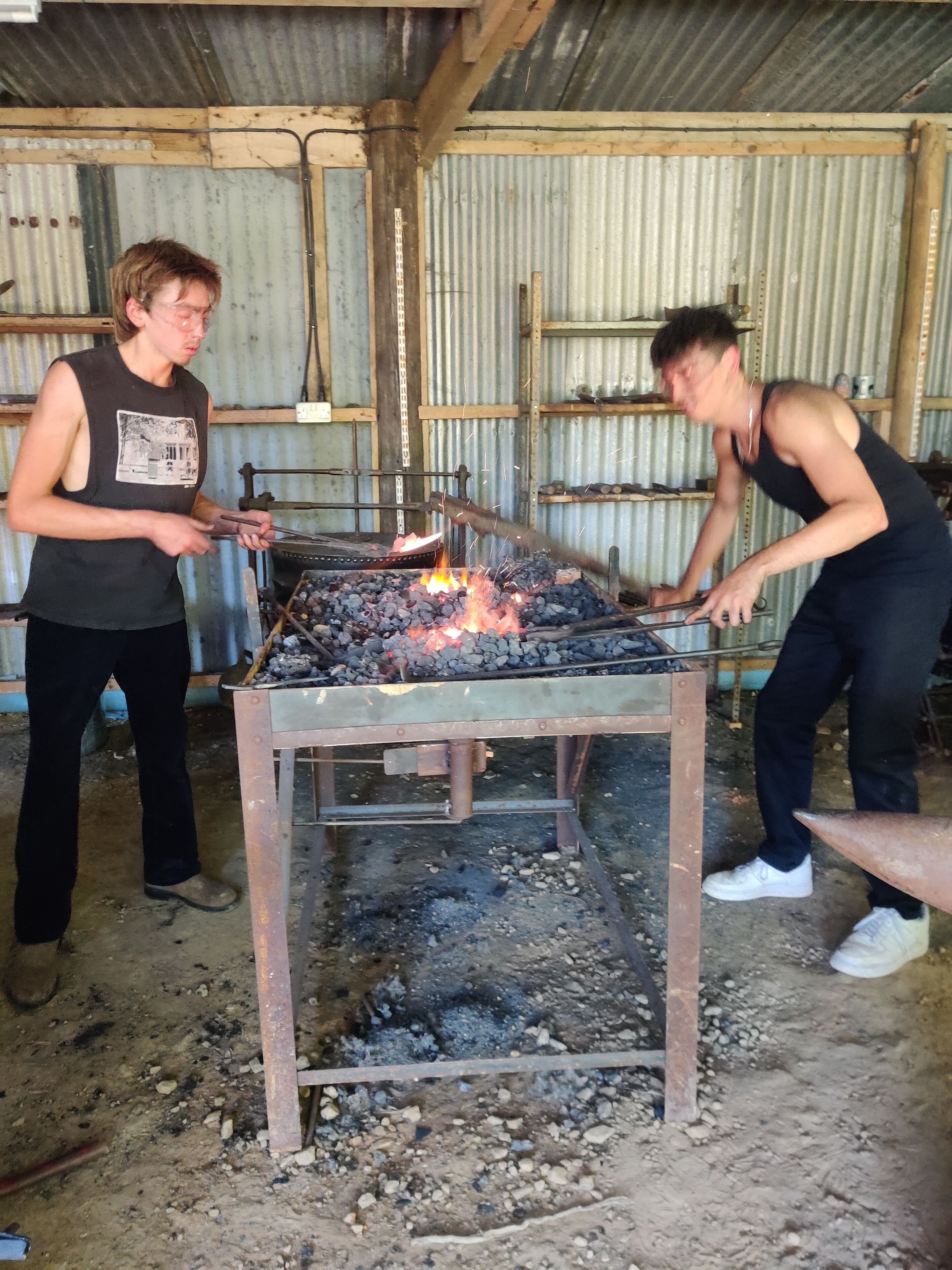 Two individuals working with a metal structure and a fire.