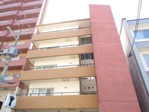 Un edificio de varios pisos con balcones, una sección de ladrillo rojo y una grúa de servicio visible.