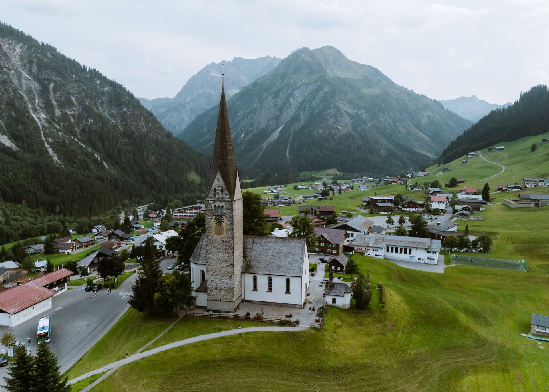Une église dotée d’un clocher imposant, entourée d’un village avec des maisons et surplombée par une montagne.