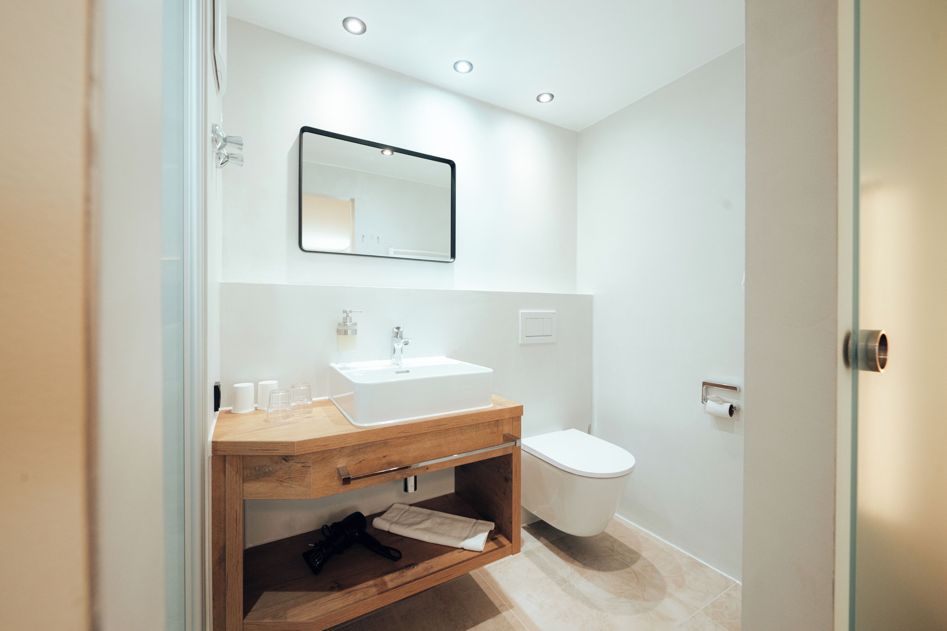 Un baño moderno con tocador de madera, lavabo blanco, espejo y retrete.
