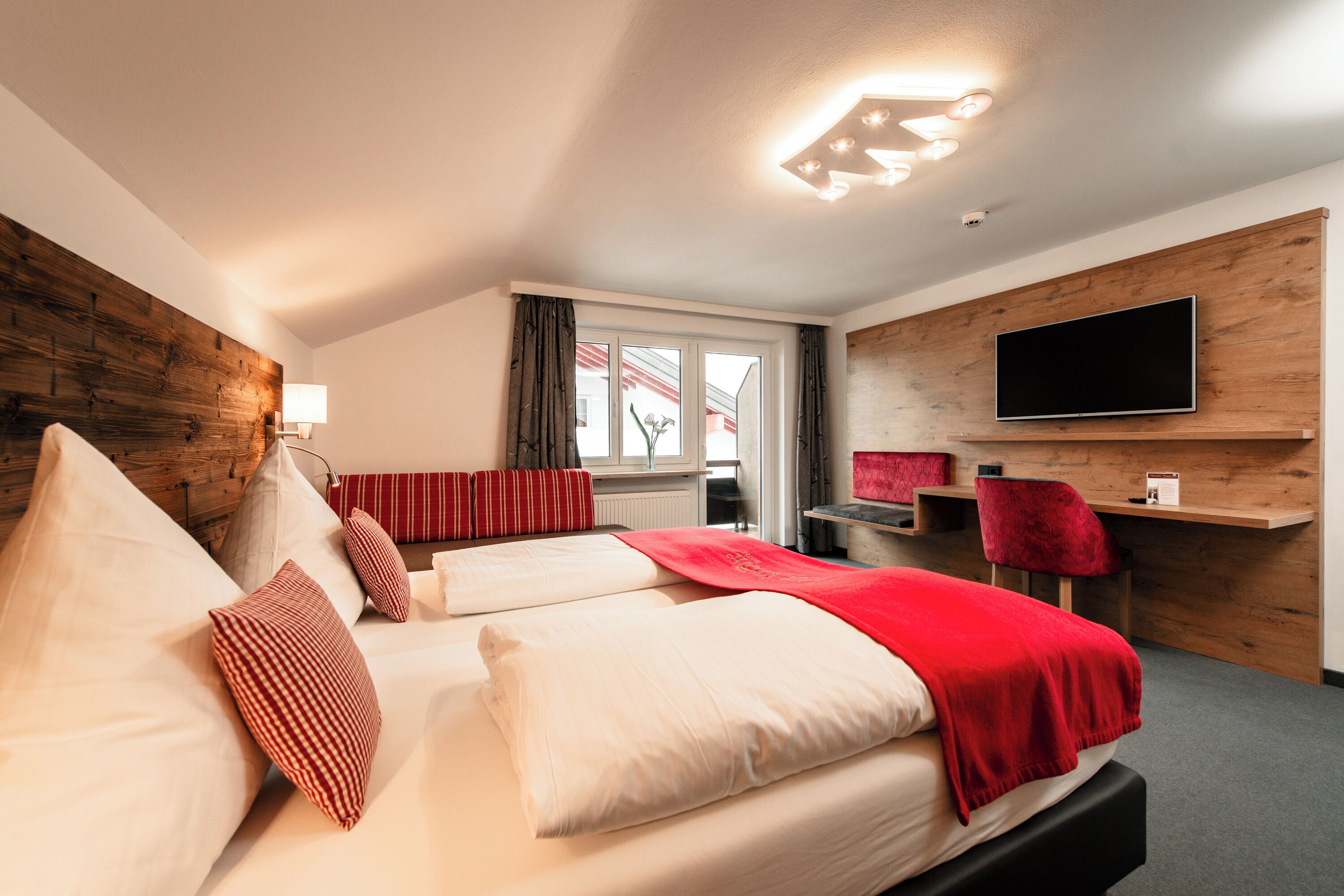 A hotel room with two beds, a TV mounted on the wall, a desk, and a window with curtains.