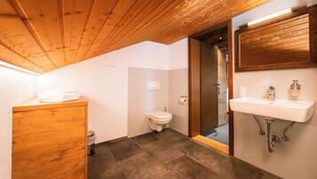 A bathroom with a wooden ceiling, a white toilet, a sink with a mirror, and a cabinet.
