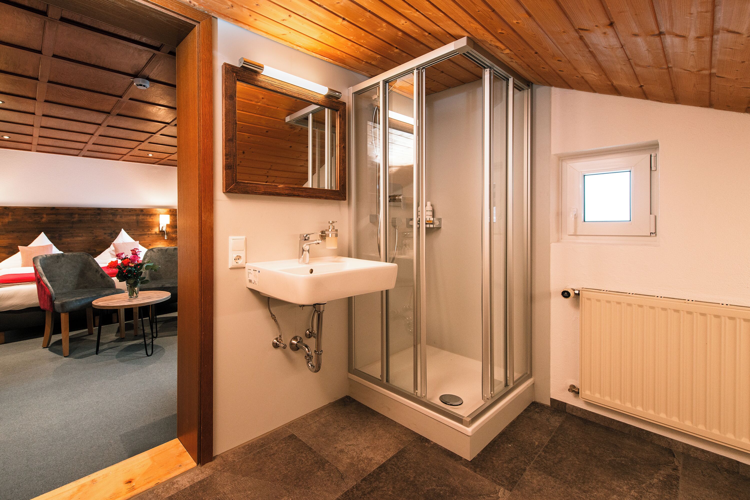 A bathroom with a glass shower, a sink, and a small window.