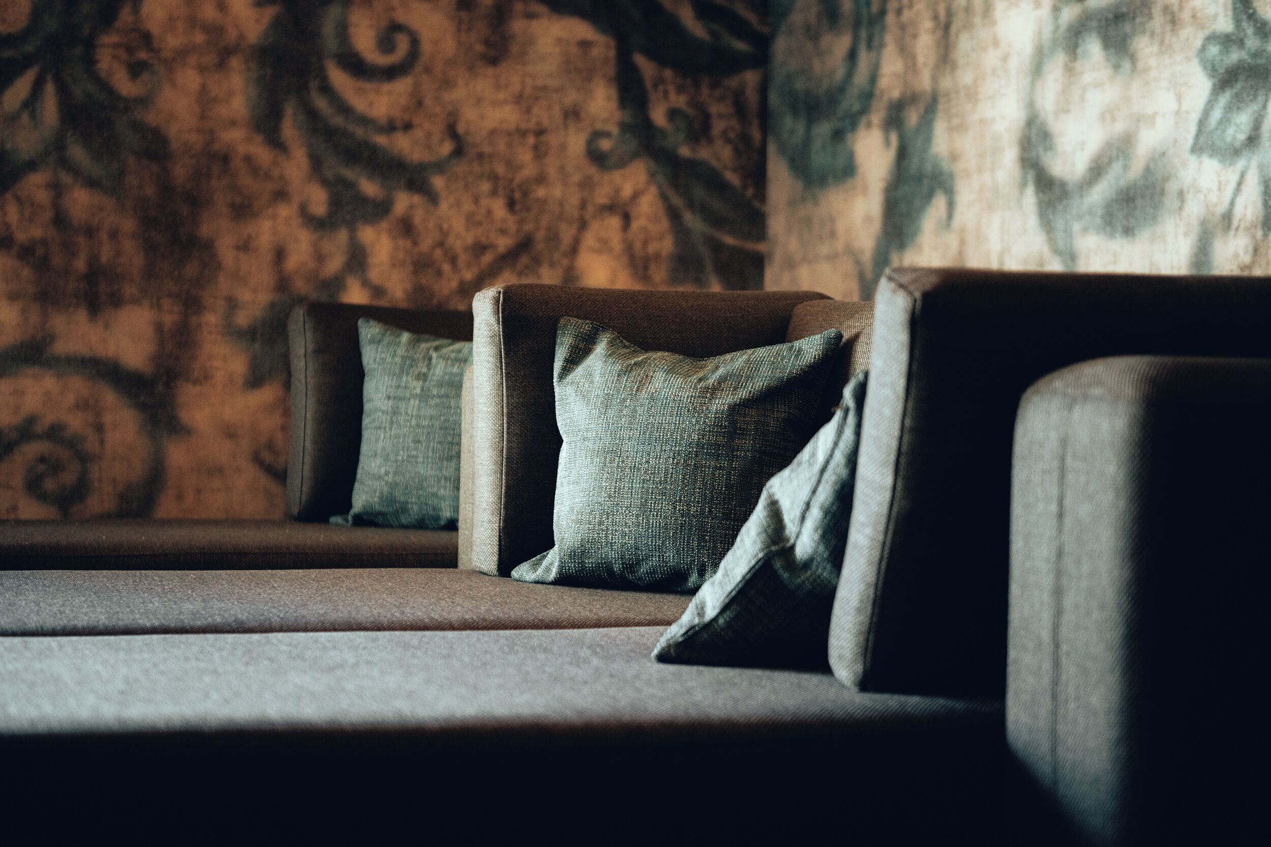 A section of a room with a sofa and cushions against a patterned wall.