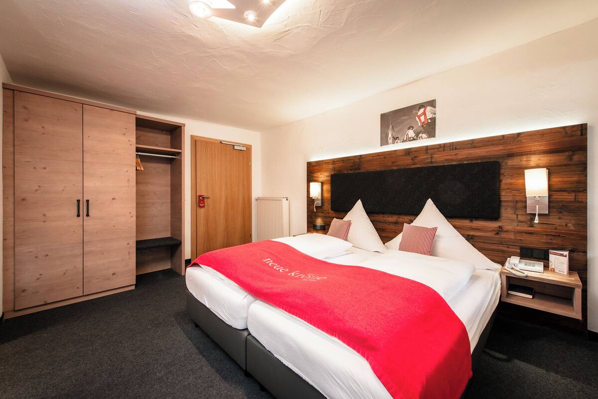 A hotel room with a large bed, a wardrobe, a bedside table with a lamp, and a wall-mounted artwork.