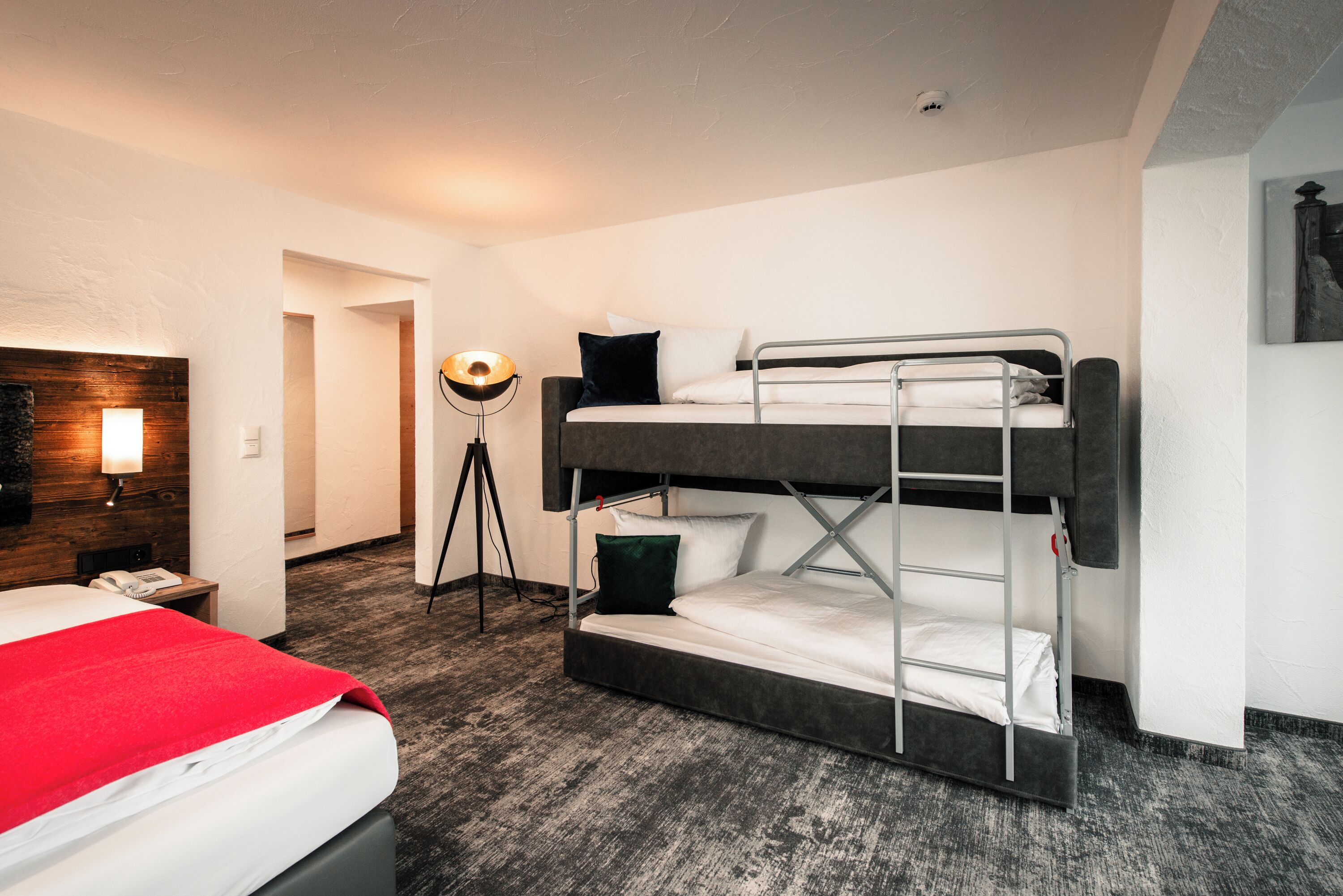 Une chambre avec un lit superposé, une couverture rouge, une lampe de chevet et une tête de lit en bois.