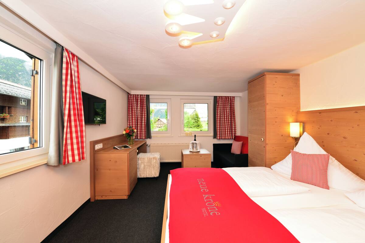 A hotel room with a bed, a desk, a chair, a small table, and a window with curtains.