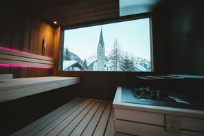 A wooden cabin interior with a window view of a snow-covered mountain and a church steeple. - Hotel Tradizio (Mittelberg)