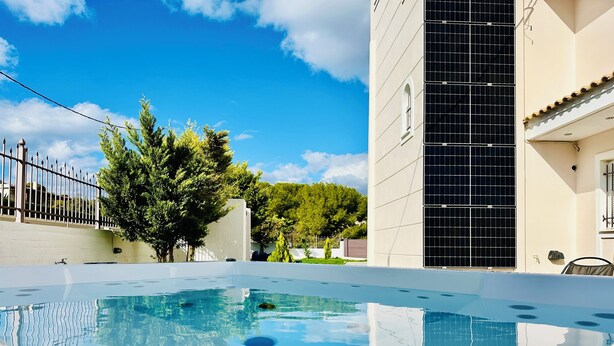 A swimming pool with clear blue water, surrounded by a white building with a tiled facade and a large window. - Airfenos - Luxury home in the Athens Riviera, Greece. (Anavissos)