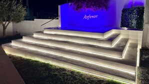 A set of illuminated outdoor steps leading to a building with a blue-lit wall and the word "Airfenos" displayed. - Airfenos - Luxury home in the Athens Riviera, Greece. (Anavissos)
