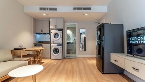 Un espace de vie compact comprenant un coin cuisine, un coin repas, un canapé, une télévision et un lave-linge.