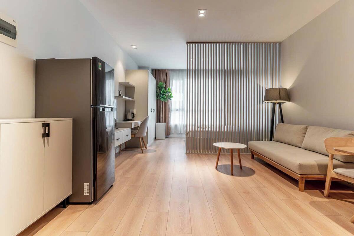 Een moderne woonkamer met een bank, een eettafel, een keuken met een koelkast, en een groot raam met verticale jaloezieën.