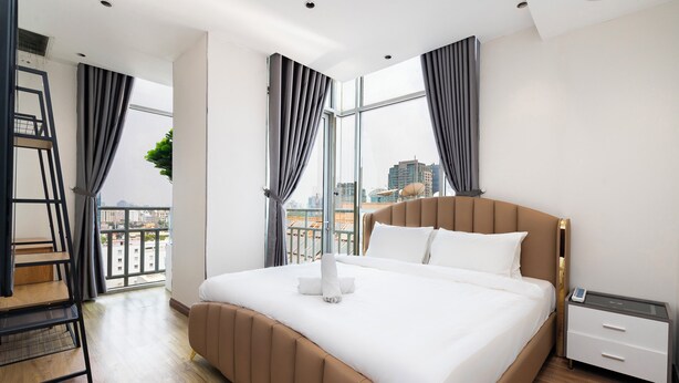 Une chambre d’hôtel moderne avec un grand lit, une table de chevet, une commode, un bureau et une fenêtre avec des rideaux.