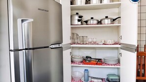 Un réfrigérateur en acier inoxydable doté d’un compartiment congélateur, ainsi qu’un meuble de cuisine avec des étagères contenant de la vaisselle, des casseroles et des ustensiles de cuisine.