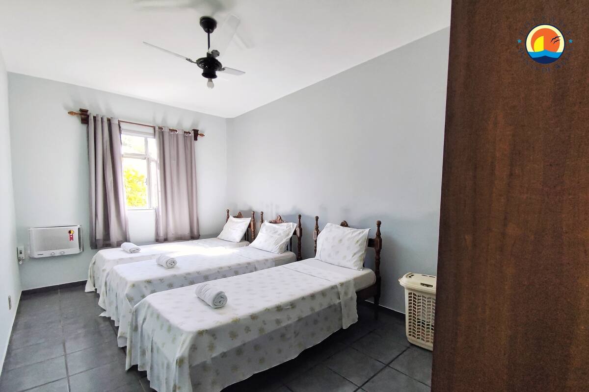 Una habitación con dos camas individuales, ventilador de techo, equipo de aire acondicionado, ventana con cortinas y suelo de baldosas.