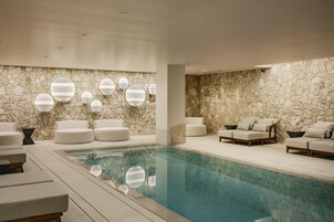 Un área de piscina interior moderna con paredes de piedra, varias zonas de estar y decoraciones geométricas en las paredes.