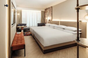 Una habitación de hotel con una cama grande, un banco, un escritorio y una silla.